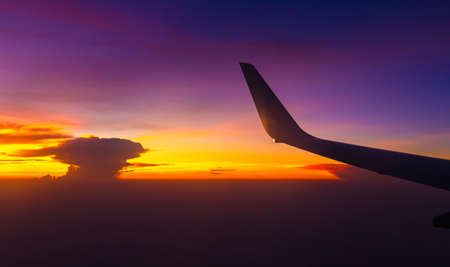 Silhouette of Airplane wing view out of the window the cloudy sunset sky background, Travel and Holiday vacation conceptの写真素材