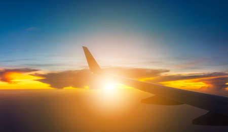 Silhouette of Airplane wing view out of the window the cloudy sunset sky background, Travel and Holiday vacation conceptの写真素材