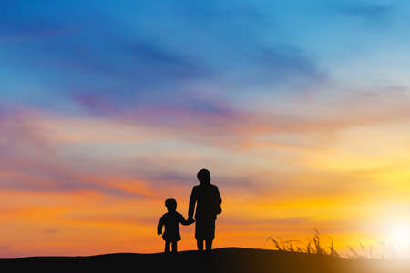 Silhouette of grandmother and grandchild looking sun down and walking on the beach evening sunset background, Happy family conceptの写真素材