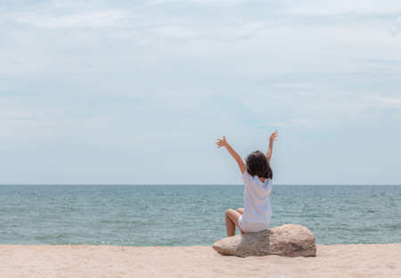 Happy little girl sitting enjoy with open arms and looking out to sea on the beachの写真素材