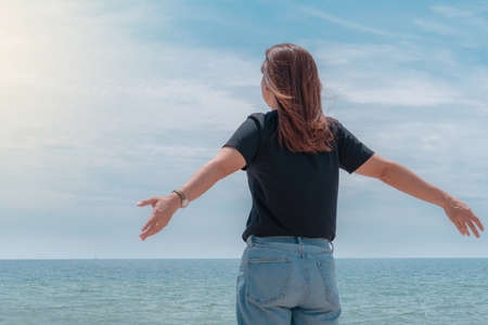 Young woman stand relaxed on beach with arms open to the sea lookingの写真素材