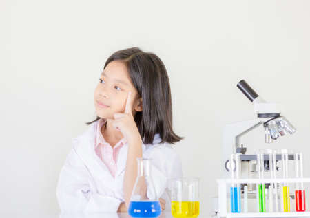 Children science concept, Happy little girl is sitting at the table and thinking at the laboratory with white backgroundの写真素材