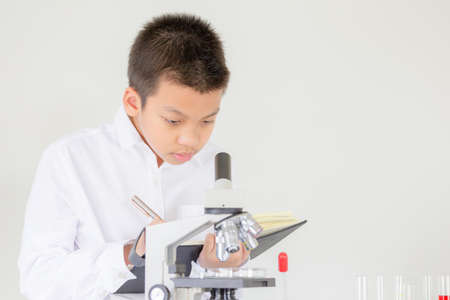Children science concept, Portrait of Kid boy using microscope in science lesson at the laboratory and recording the resultsの写真素材