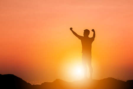 Silhouette of Man Celebration Success Happiness on a Stone Evening Sky Sunset at Beach Background, Sport and active life Concept.の写真素材