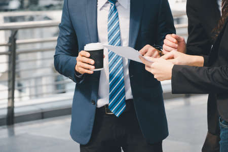 Businessman and business woman walking outside office with paper sheet and coffee cup in hand.の写真素材