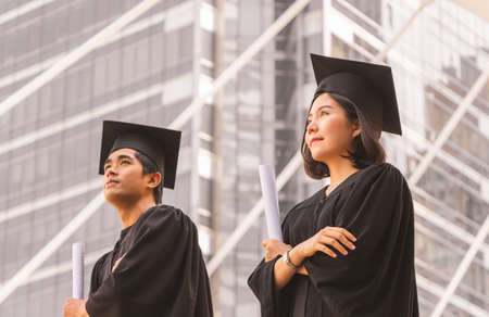 Close up of graduate student holding a diploma and looking into the sky, Education concept.の写真素材