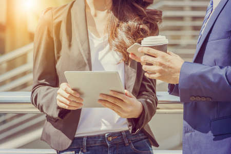 Close up of young businesswomen and smart business man with smartphone and coffee cup in handの写真素材