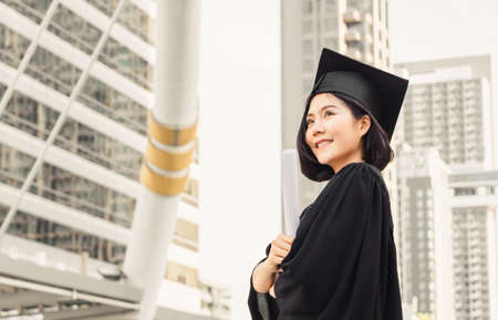 Close up of graduate student holding a diploma and looking into the sky, Education concept.の写真素材