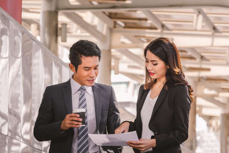 Businessman and business woman walking outside office with paper sheet and coffee cup in hand.の写真素材