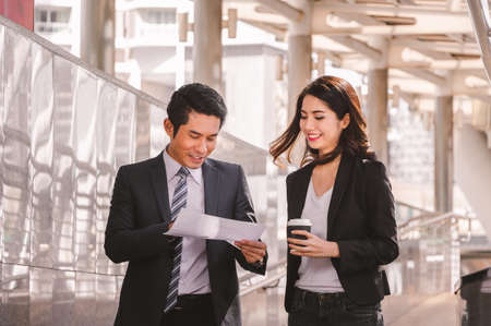 Businessman and business woman walking outside office with paper sheet and coffee cup in hand.の写真素材