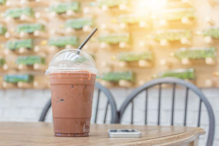 Iced cocoa in takeaway cup and smartphone on table in coffee shopの写真素材