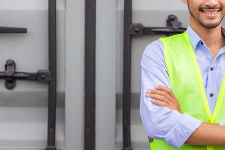 Cheerful engineer man in hard hat with arms crossed at cargo containerの写真素材