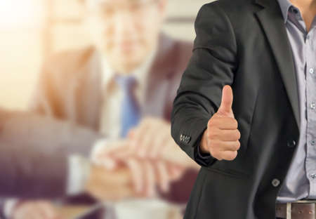Businessman giving thumb up as sign of Success over blurred business people team backgroundの写真素材