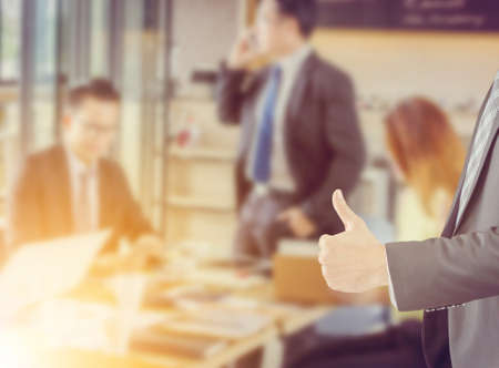 Close up of Businessman giving thumb up as sign of success over blurred business people team backgroundの写真素材