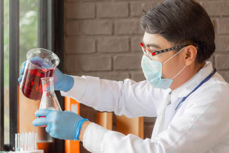 Doctor analyzing medical test tubes examining beaker with red fluid in laboratoryの写真素材