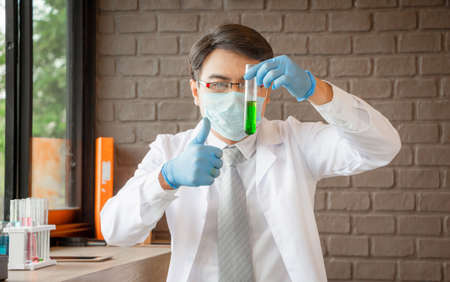 Doctor analyzing medical test tubes examining beaker with green fluid, Scientist giving thumb up as sign of success in a laboratory, Covid-19 conceptの写真素材