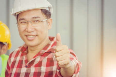 Close up of Smiling business engineer man giving thumb up as sign of success over blurred people team at construction site backgroundの写真素材