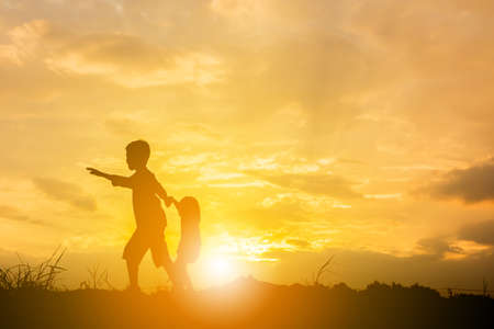Silhouette of Boy and girl playing at sunset background, Happy children concept.の写真素材