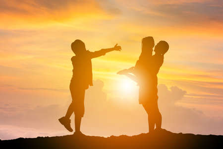 Silhouettes of mother daughter and son playing at sunset evening sky backgroundの写真素材