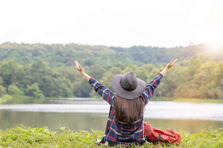 Young traveler woman with black hat in hipster style sitting relax at lake blurred backgroundの写真素材