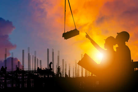 Silhouette of Engineer and worker on building site, construction site sunset in evening time.の写真素材