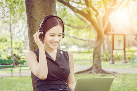 Beautiful young woman with headphones and laptop enjoys and relaxed in music in the parkの写真素材