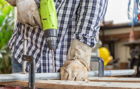 Selective focus of The carpenter is using drill to mae hole in wooden plank working in carpenters shopの写真素材