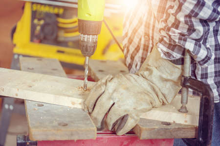 Close up of The carpenter is using drill to mae hole in wooden plank working in carpenters shopの写真素材