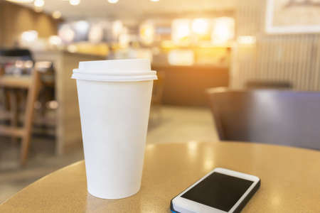 Disposable hot coffee cup with smartphone on a wooden table in coffee shop backgroundの写真素材