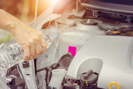 Close up of women hand fill fresh water into windscreen or in water tank wiper on car engine room,...