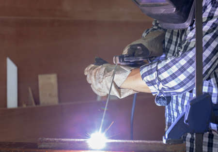 Worker in workwear welding the steel part by manual with safety equipment