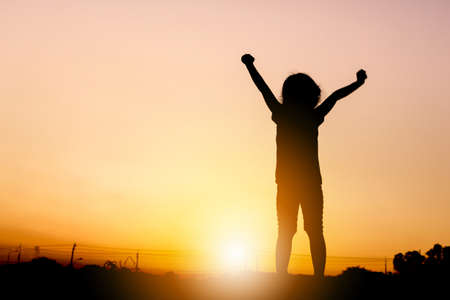 Silhouettes of little girl playing at sunset evening sky background.の写真素材