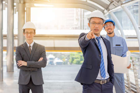 Business team engineer planing with white helmet and holding drawing paper in hand against city background planing and teamwork management conceptの写真素材