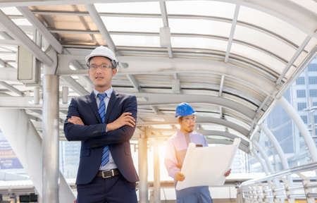 Business team engineer planing with white helmet and holding drawing paper in hand against city background planing and teamwork management conceptの写真素材