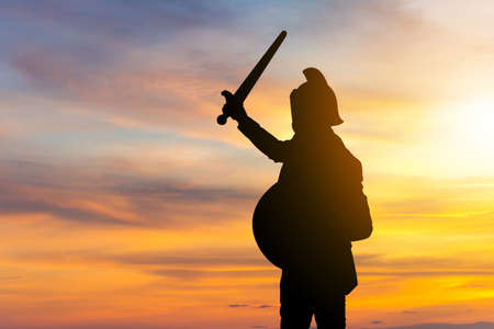 Silhouette of Businessman Knight Sword and Shield in Sunset Background, Fighting Business Warrior Concept.の写真素材