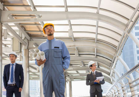 Business team engineer planing with white helmet and holding drawing paper in hand against city background planing and teamwork management conceptの写真素材