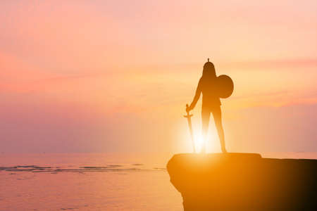 Silhouette of Business woman Knight Sword and Shield in Sunset Background, Fighting Business Warrior Concept.の写真素材