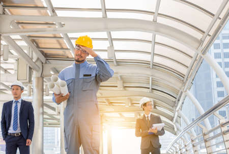 Business team engineer planing with white helmet and holding drawing paper in hand against city background planing and teamwork management concept.の写真素材