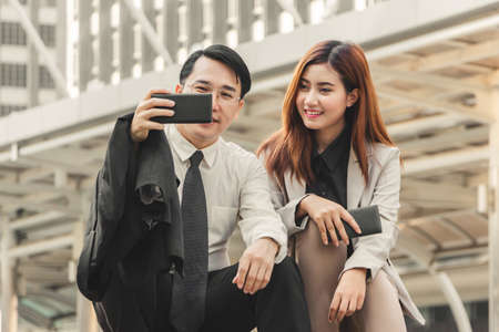 Joyful businessman and woman taking a selfie while sitting together at stairsの写真素材