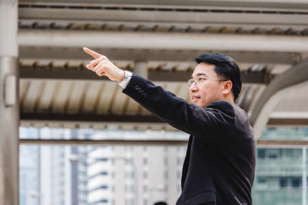 Portrait of businessman standing outside office and pointing to the skyの写真素材