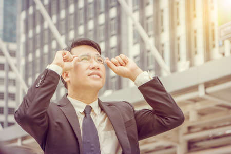 Portrait of business man standing outside office and looking the sky.の写真素材