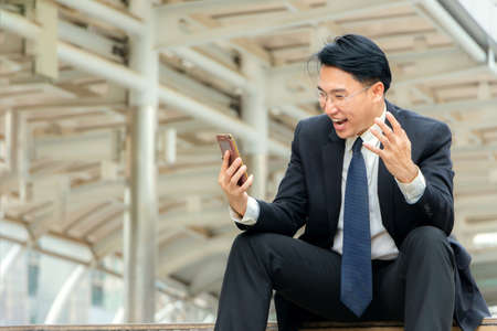 Business man looking at his smartphone and satisfied while have good newsの写真素材