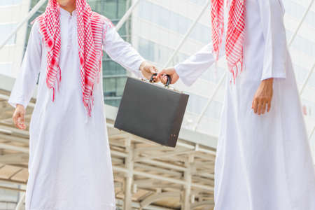 Close up of two male hands young Arab Middle Eastern business man holding black leather briefcase...