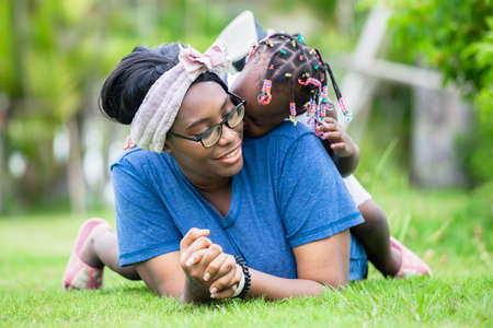 Cheerful african american girl playing on the back of her mother, Happy mother and daughter laughing together outdoorの写真素材