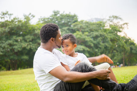 Happy African American father while hug and carry his son, Dad was kissing his son in the park, Joyful black family concept.の写真素材