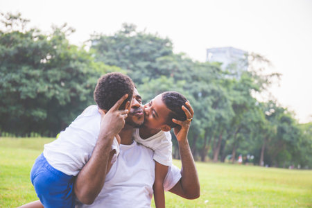 African Cute little boy in casual kissing dad at park. Happy African American father playing...