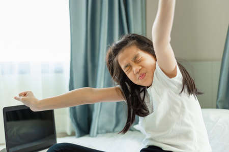 Asian little kid stretching in bed after studying online, girl relaxing after finish distance learningの写真素材