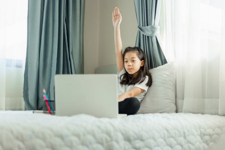Asian little kid sittinh on bed studying online , girl student learning online class from school teacher.の写真素材