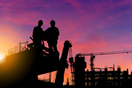 Silhouette of Engineer and worker checking project at building site background, construction site at sunset in evening timeの写真素材