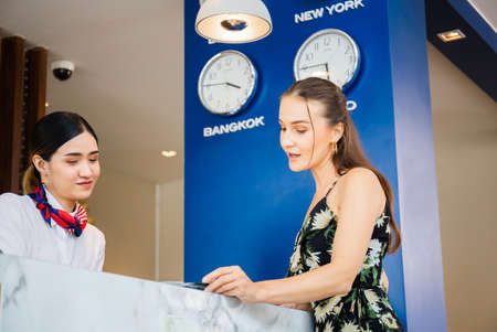 Happy guest and receptionist at hotel reception, Young travellers standing at reception desk with female receptionist standing at hotel counterの写真素材